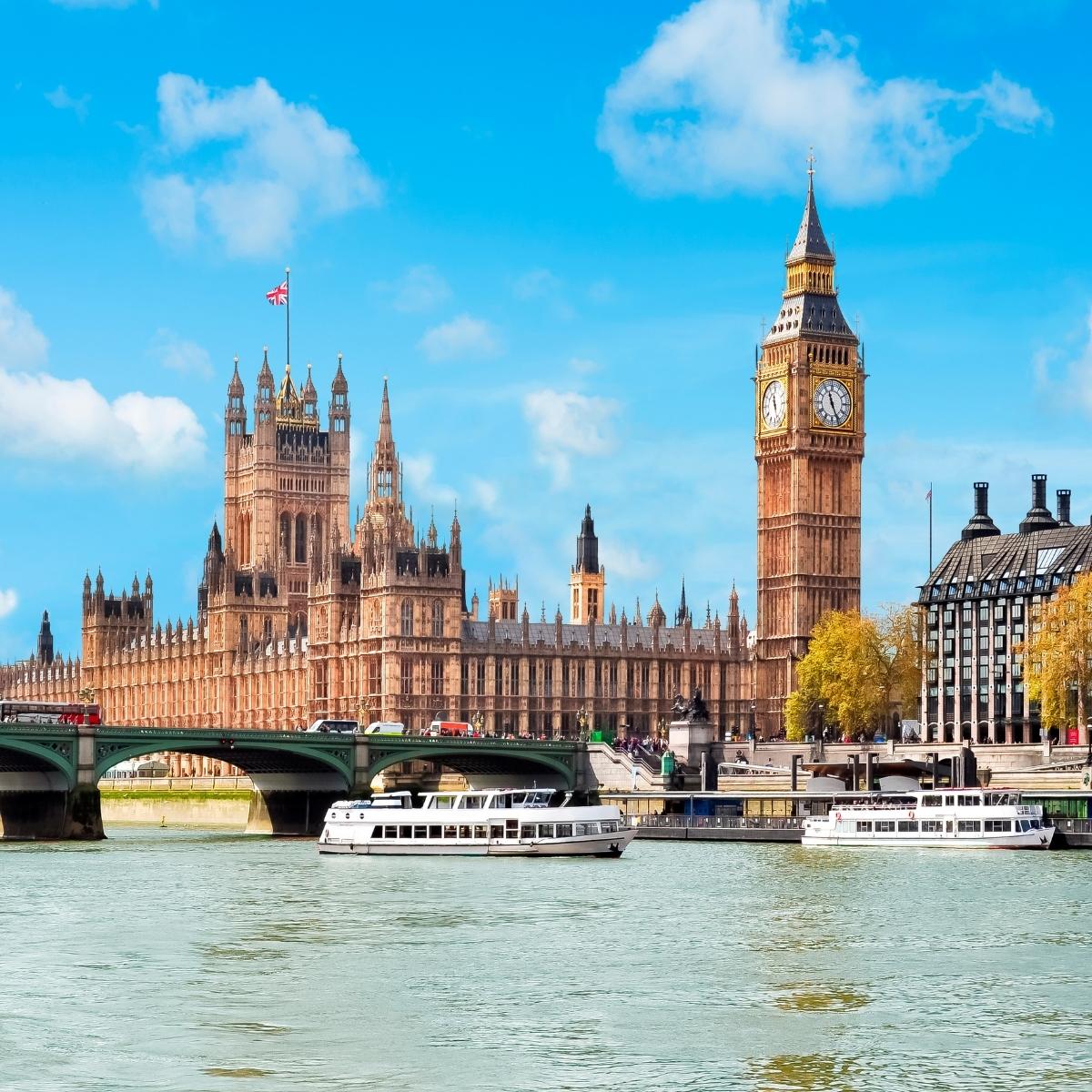 The Houses of Parliament and Big Ben in London are seen across the River Thames on a clear day, with boats on the water and Westminster Bridge in the foreground—a classic view often enjoyed on London walking tours.