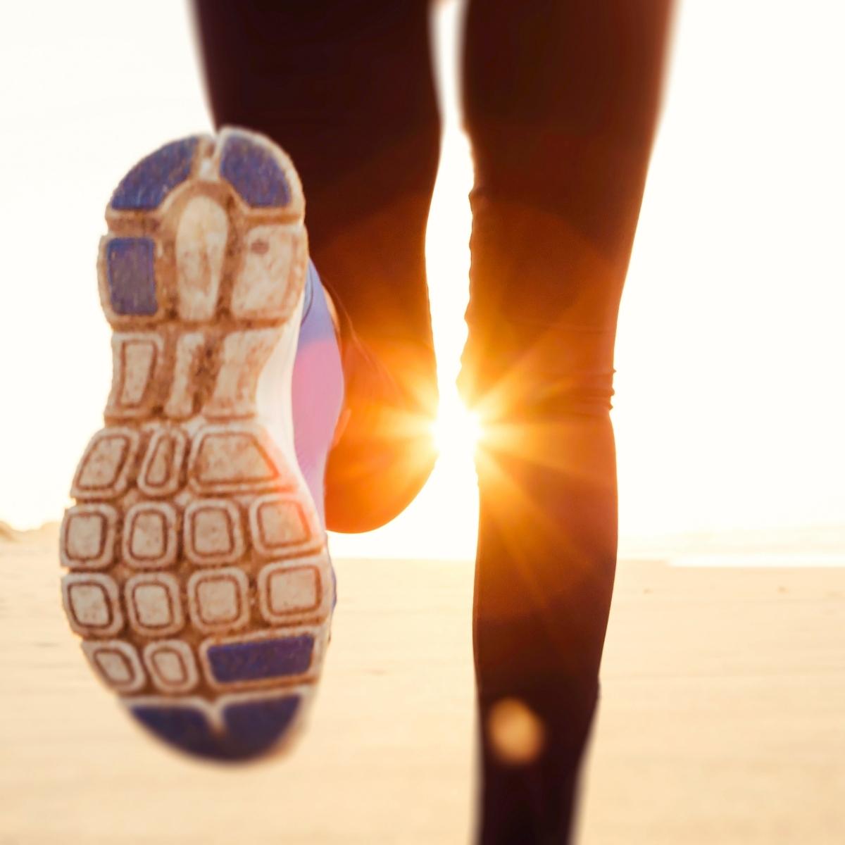 Close-up view of a person's running shoe sole as they run outdoors on a sandy surface with the sun shining brightly, perfect for exercise or testing gear like the Buddy Pouch—ideal for your next outdoor running review.