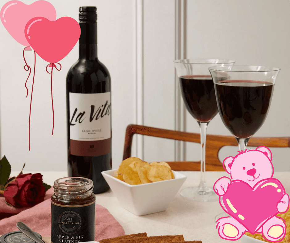 A table set for romance with wine, snacks, and a rose—plus balloons and a teddy bear holding a heart. Enter to win a Valentine's hamper and make your celebration extra special!.