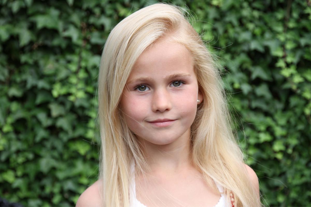 young girl outside smiling with a bush behind her