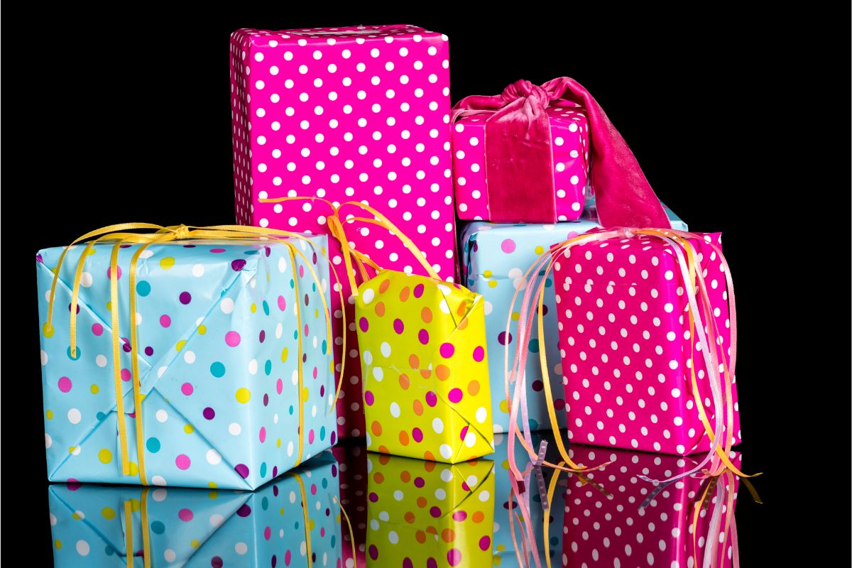 Five gift boxes wrapped in colorful, polka-dotted paper with ribbons are arranged on a reflective black surface—perfect gifts for teenagers. The pink, blue, and yellow boxes each feature unique ribbon styles and playful polka dot patterns.