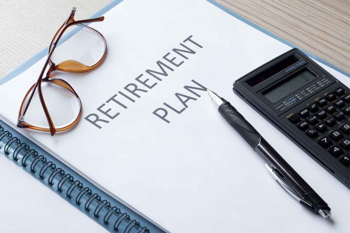 A document labeled "Retirement Plan" sits on a desk, surrounded by eyeglasses, a pen, a calculator, and a spiral notebook—tools essential for mapping out retirement strategies and ensuring financial well-being.