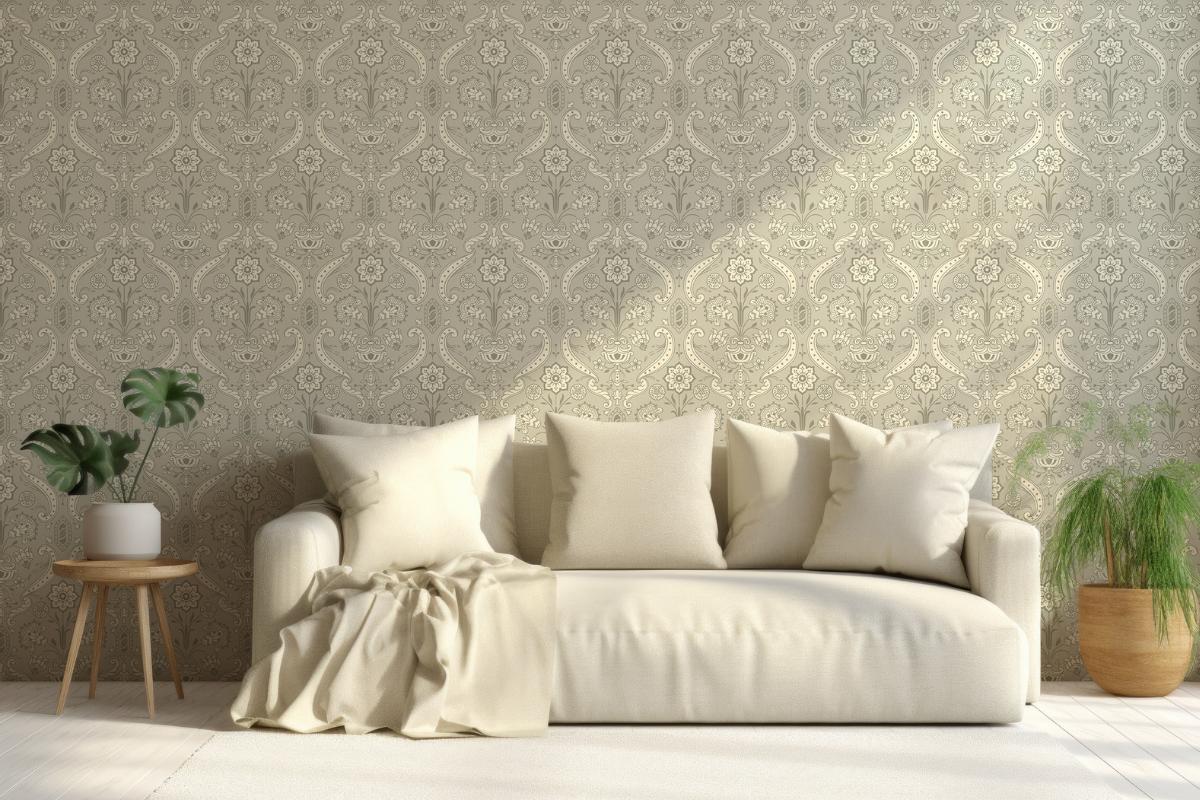 A cream-colored sofa with four pillows and a draped blanket sits against patterned beige wallpaper. A small table with a potted plant—perfect for trying new indoor plant care tips—is on the left, and a larger potted plant is on the right.