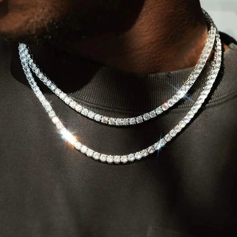 A close-up of a young man in a plain black shirt, wearing two layered, sparkling diamond tennis necklaces that catch the light—prom jewellery designed to truly stand out.